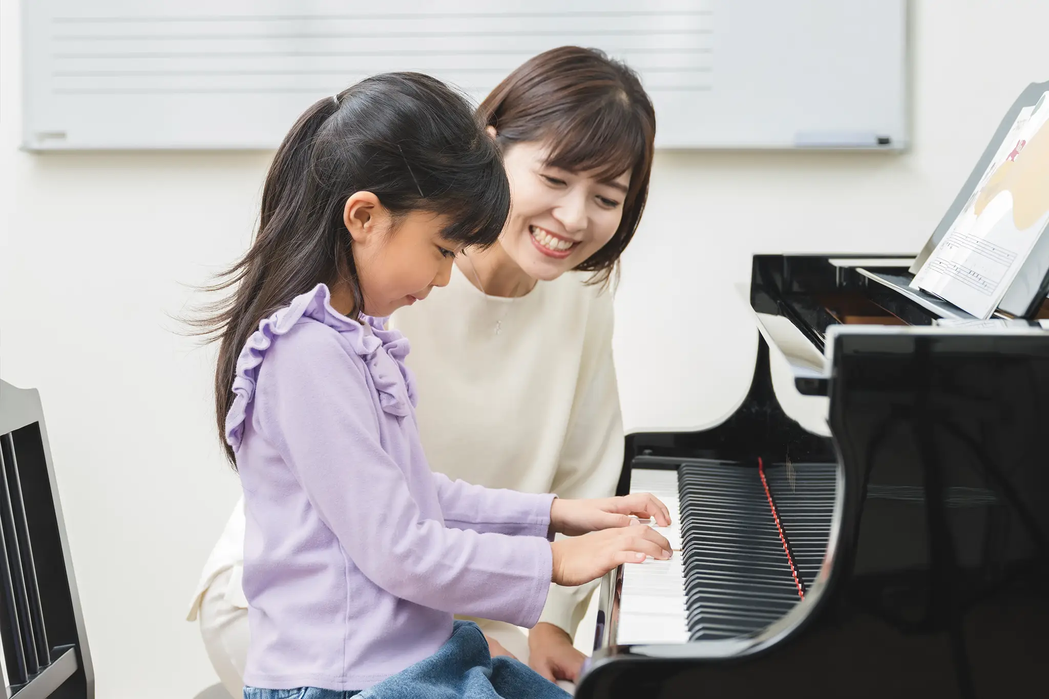Yamaha music school teacher smiling and teaching young child to play piano